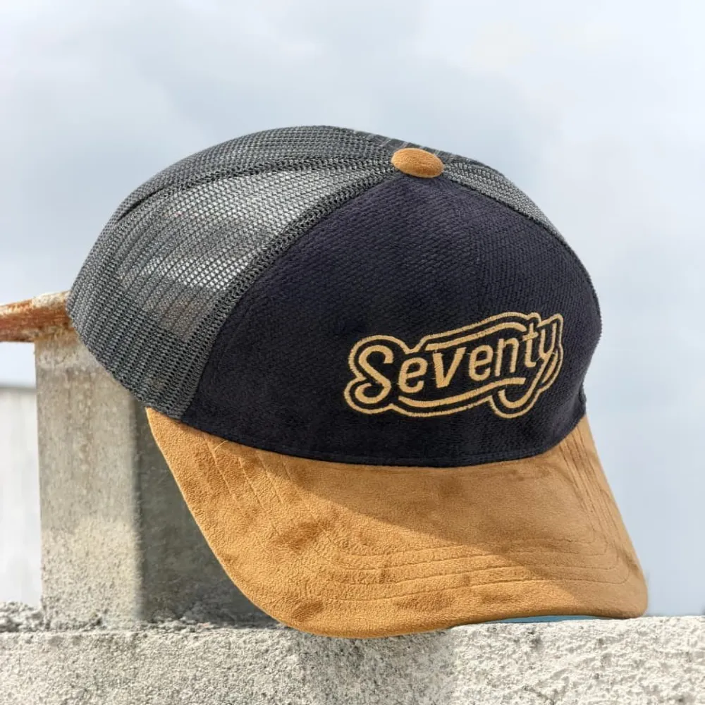 11Sports rose corduroy trucker cap with white mesh and a mountain Seventy patch on a tree branch.