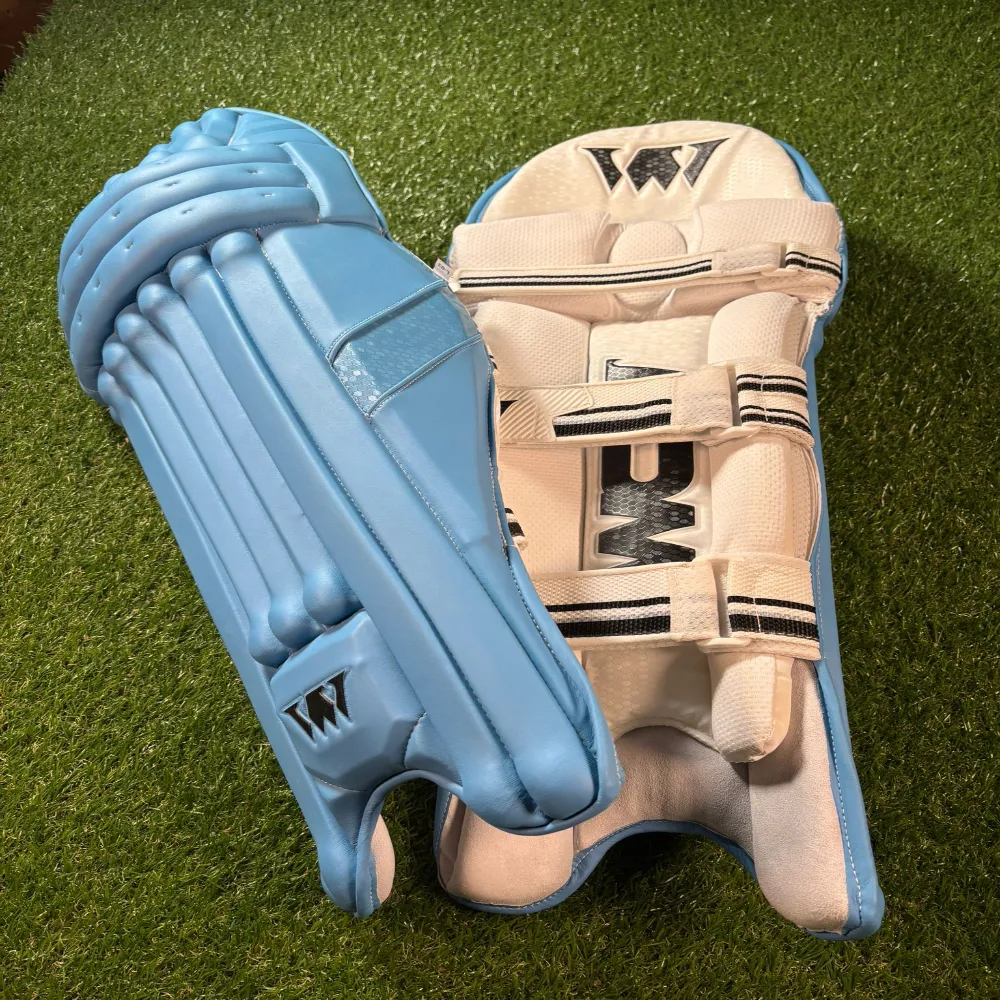 11Sports powder blue cricket batting pads resting on artificial grass showing front face and inner bolster.