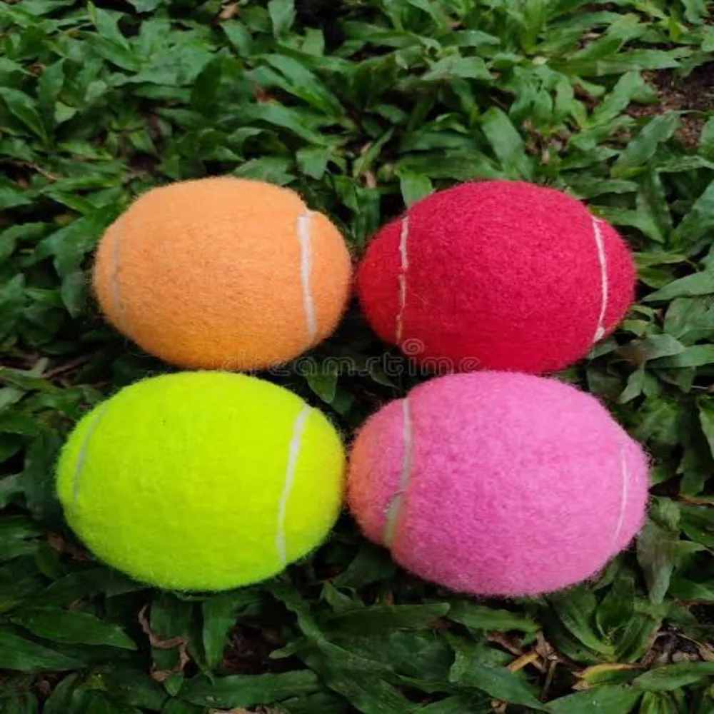 Four 11Sports tennis cricket balls in orange, red, yellow, and pink resting on grass.