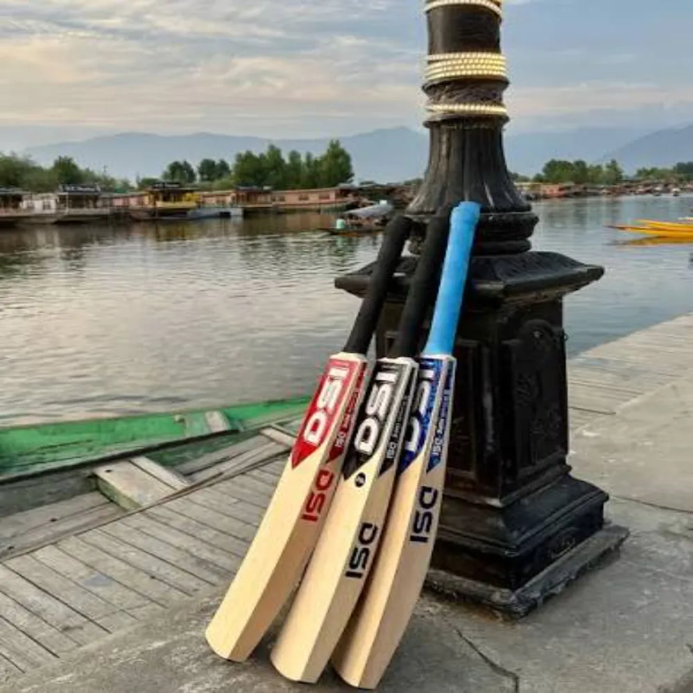 Three 11Sports DSI Kashmir willow cricket bats leaning on an antique lakeside lamp post with boats in the background.